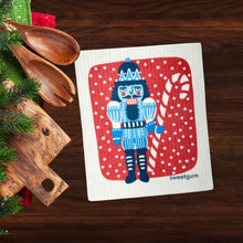 Load image into Gallery viewer, Blue Nutcracker Swedish Dishcloth | Red background with snow